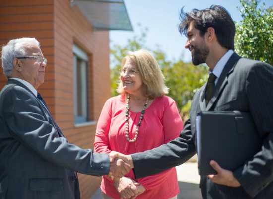 Real estate agent and mature couple shaking hands outdoors, sealing a deal with smiles.